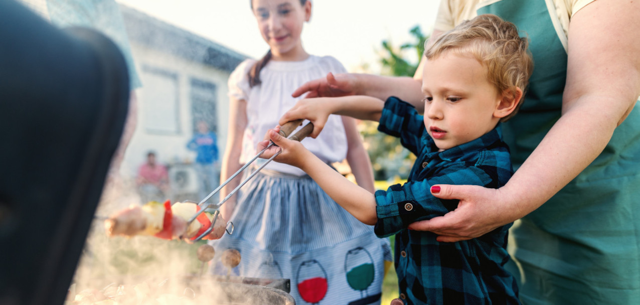 Eine Frau zeigt Kindern den Umgang mit Feuer beim Grillen