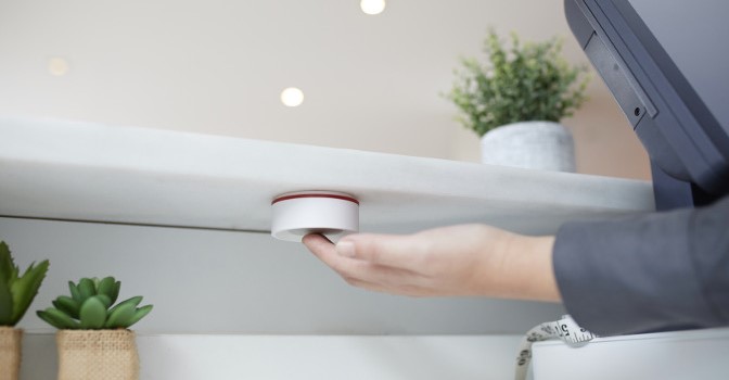 Mitarbeiter an der Kasse drückt Notfalltaste mit stillem Alarm